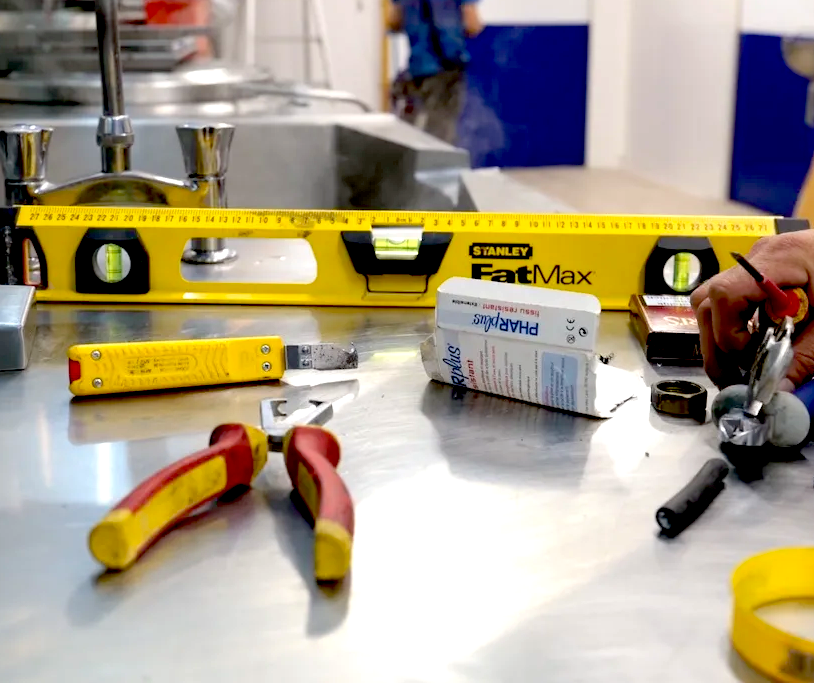 des outils de chantier jaune pince cutter niveau sur un plan de travail en inxo dans une cuisine
